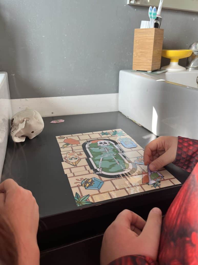 Mains d'un enfant qui reconstitue un plateau de jeu d'Halloween imprimé, à côté d'un crâne