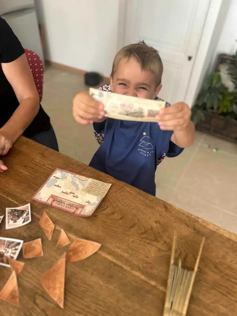 Un petit garçon brandit fièrement le billet qu'il vient de trouver, les pièces du tangram sur la table, pendant L'affaire des bijoux volés