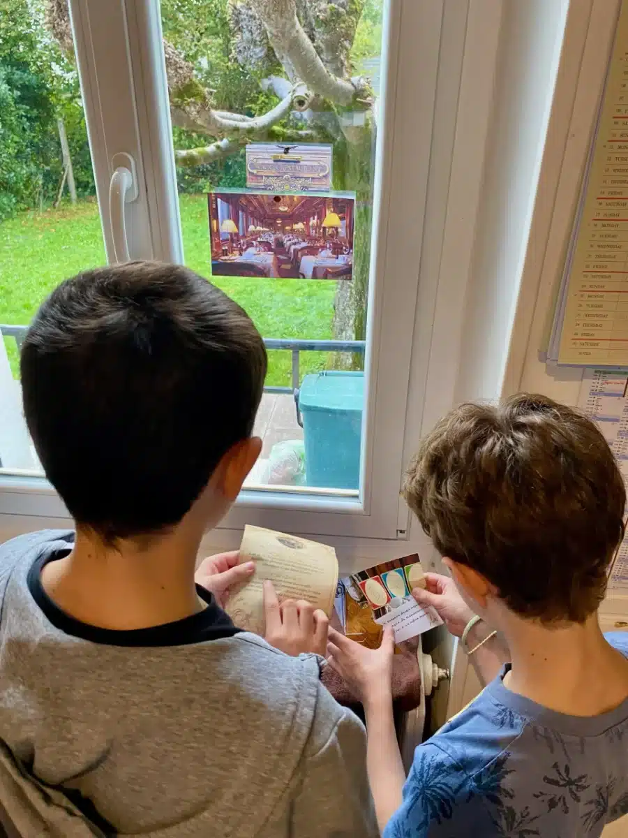 Deux garçons déchiffrent un indice devant la fenêtre pendant l'escape game en famille L'affaire des bijoux volés