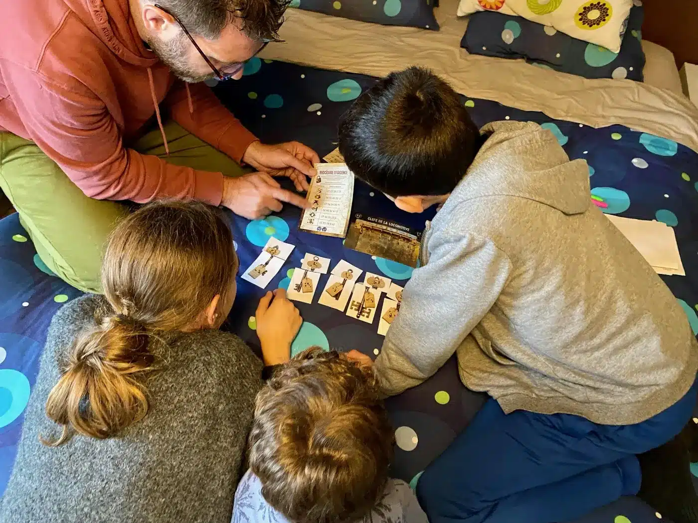 Un père et trois enfants assis par terre résolvent les énigmes de L'affaire des bijoux volés, un escape game en famille