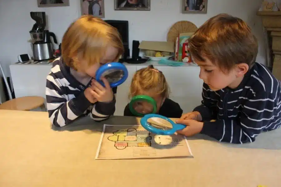 Trois enfants observent une énigme à la loupe autour de la table de la cuisine