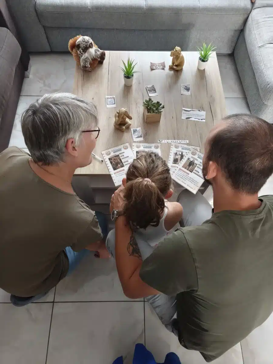 Une grand-mère, un père et une petite fille enquêtent autour de la table du salon pendant l'escape game en famille Mission Safari