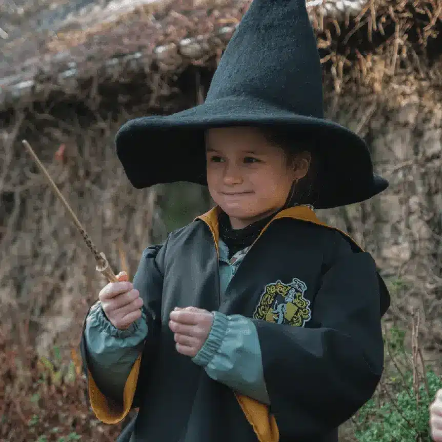 Enfant en robe de sorcier et chapeau pointu, baguette à la main, pendant un jeu d'enquête sur le thème des sorciers